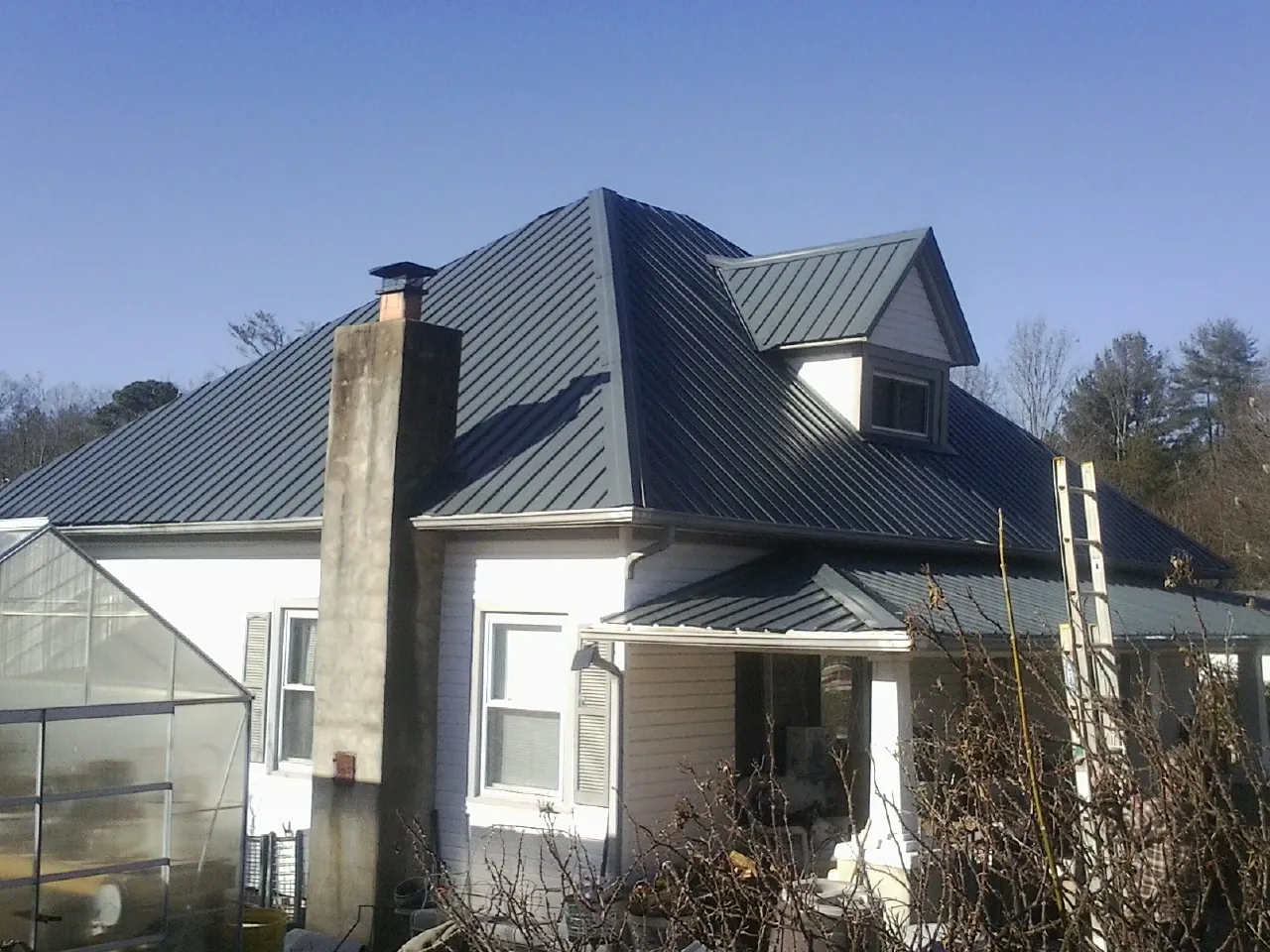 Dark blue standing seam metal roof on a white farmhouse with dormer — Slate & Tile Roof Repair by Roofing Brothers in Calypso