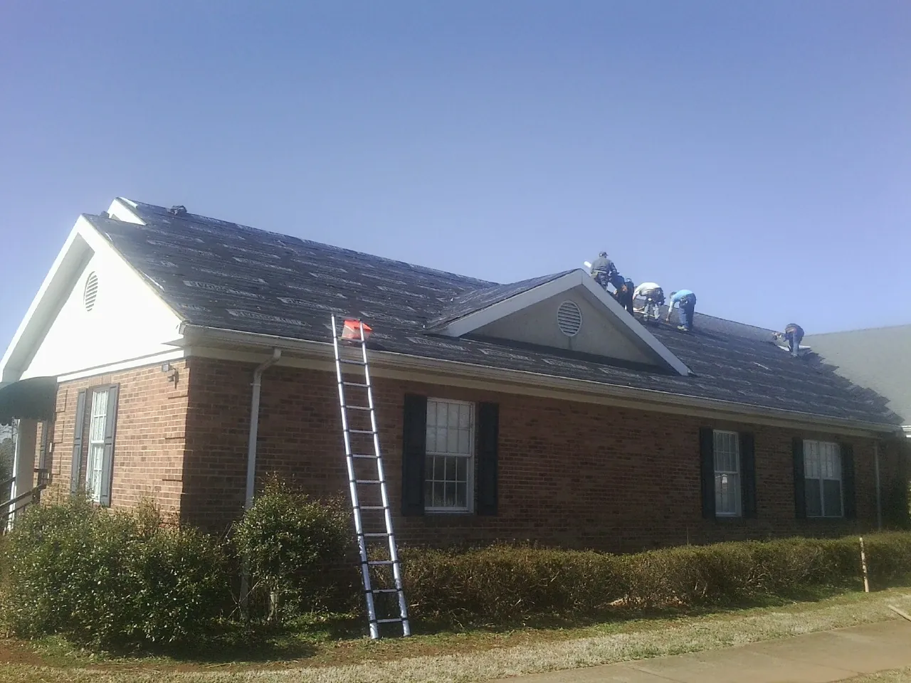 Crew tearing shingles off a brick ranch roof with a ladder set — Emergency Roof Repair work by our crew in Calypso