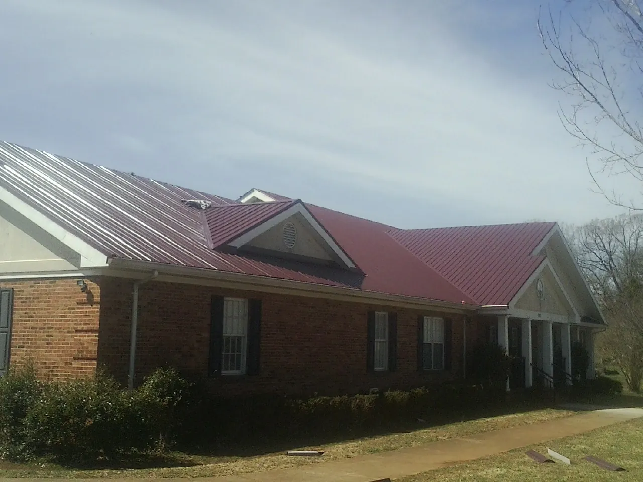 Red metal roof with gabled entries on a long brick building, from a Hail Damage Roof Repair job in Calypso