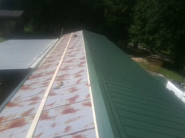 Old rusted panels beside newly installed green metal roofing — Wind Damage Roof Repair by Roofing Brothers in Calypso