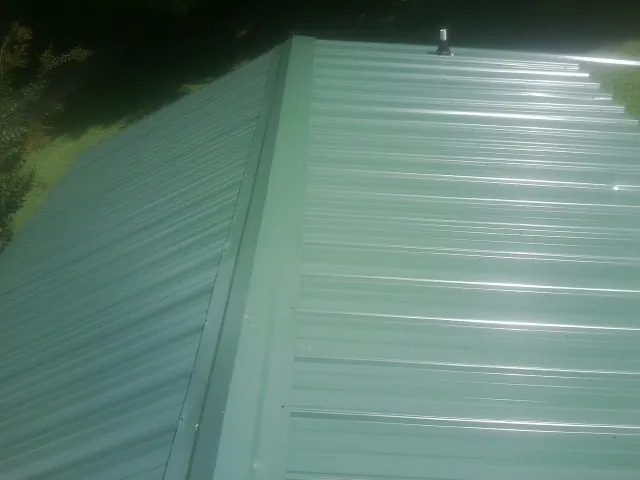 New green metal panels meeting at the ridge of a roof — Flat Roof Repair work by our crew in Calypso