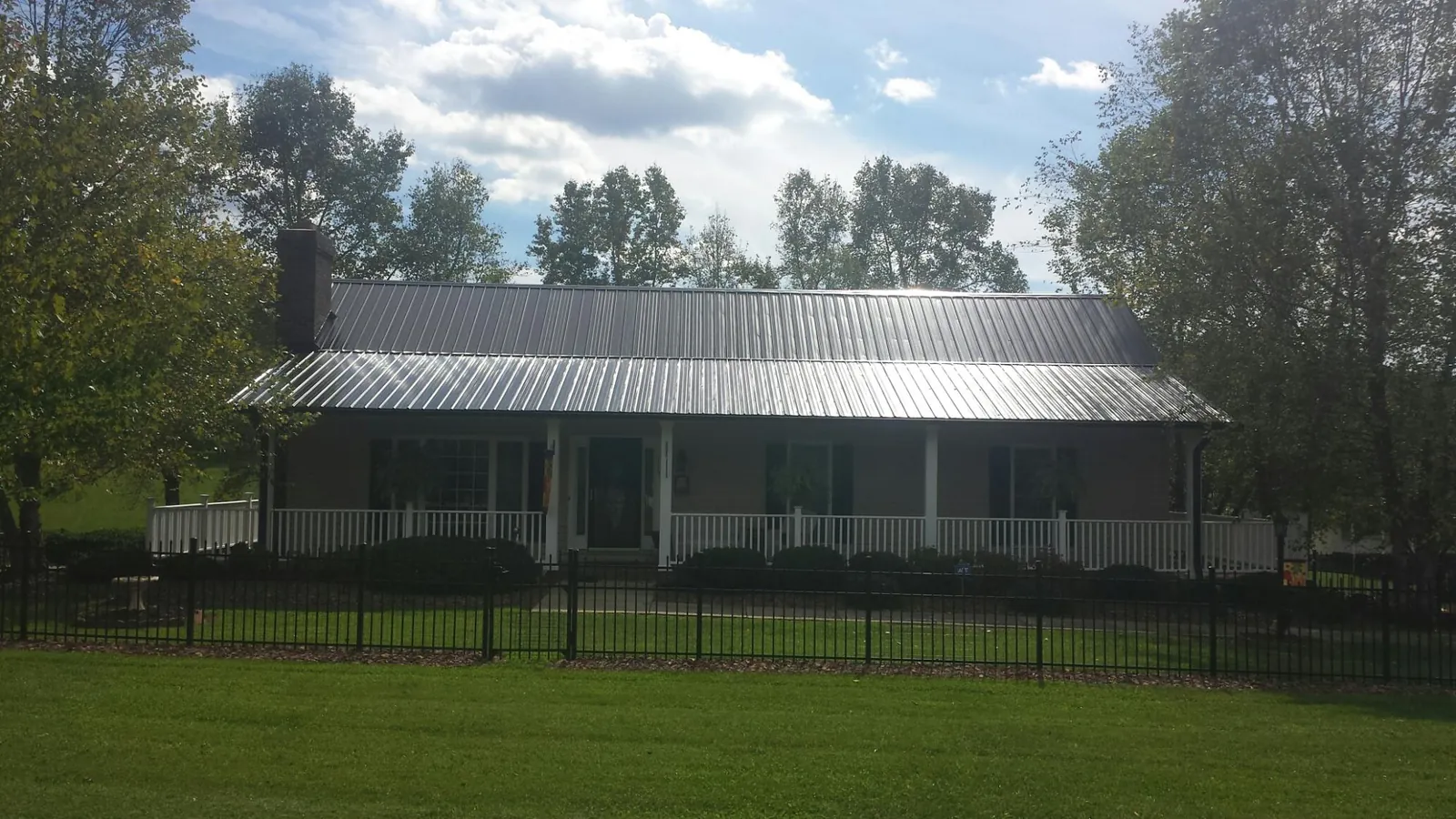 Gray metal roof on a brick ranch with a full width front porch — Gutter Guard Installation work by our crew in Calypso